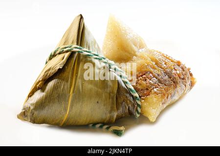 Nahaufnahme eines gedämpften chinesischen klebrigen Reisknödlings, Zongzi oder Bakcang und eines weiteren, noch in Bambusblatt gewickelt, im Hintergrund Stockfoto