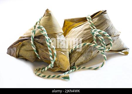 Zwei klebrige chinesische Reisknödel, Zongzi oder Bakcang, in Bambusblätter gewickelt, auf weißem Hintergrund Stockfoto