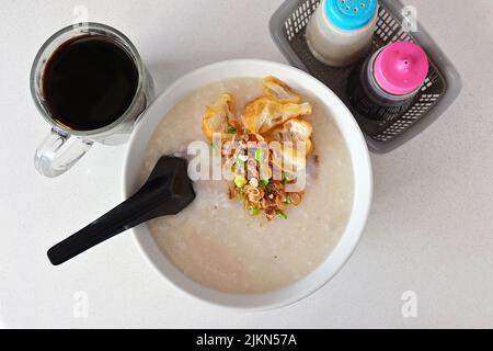 Kantonesisches Ting Zai Porridge oder „Congee on the Boat“, mit einer Tasse traditionellen schwarzen Kaffee, ein beliebtes Frühstück in Südostasien Stockfoto