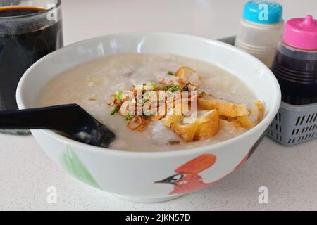 Kantonesisches Ting Zai Porridge oder Congee, mit einer Tasse traditionellen schwarzen Nanyang-Kaffee, einem klassischen, komfortablen Frühstück in Südostasien Stockfoto