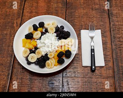 Gesunde Mahlzeit zum Frühstück oder Mittagessen Schüssel mit Quark und Obst, bestehend aus Bananenscheiben, Heidelbeeren und Brombeeren, Blick von oben. Stockfoto