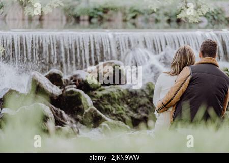 Rückansicht eines Paares, das im Herbst am Flussufer im Park sitzt Stockfoto