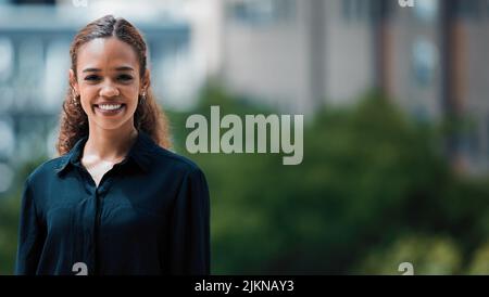 Jung und innovativ. Eine junge Geschäftsfrau, die sich vor städtischem Hintergrund posiert. Stockfoto
