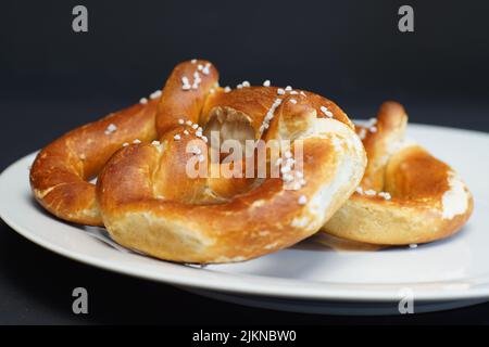 Eine Auswahl frisch gebackener, weicher Brezel auf einem weißen Teller auf grauem Hintergrund Stockfoto