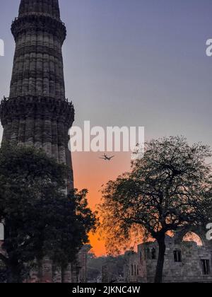 Eine wunderschöne Aussicht auf einen alten Qutab Minar Turm und ein Flugzeug, das in den Himmel fliegt Stockfoto