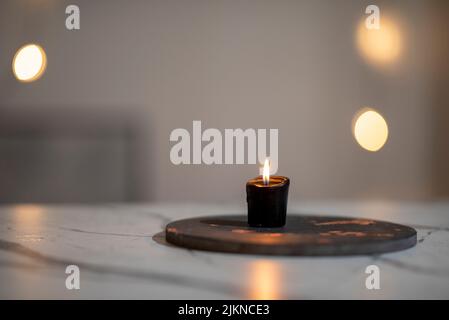 Eine Nahaufnahme einer brennenden schwarzen Kerze auf einem weißen Marmortisch auf einem unscharfen Bokeh-Hintergrund Stockfoto
