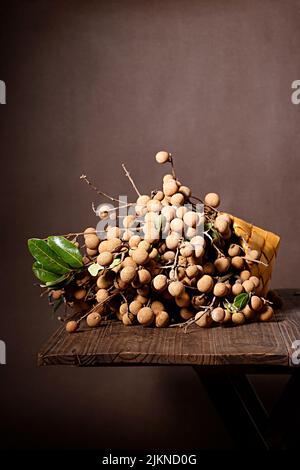 Eine vertikale Nahaufnahme von Longan auf dem Holztisch isoliert auf braunem Hintergrund. Stockfoto