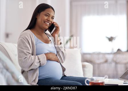 Das Baby wird jedes Mal aufgeregt, wenn Sie anrufen. Eine Schwangere spricht auf ihrem Handy, während sie zu Hause auf dem Sofa sitzt. Stockfoto