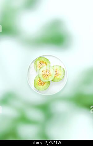 Eine selektive Fokusaufnahme von geschnittener grüner Melone auf einem weißen Teller auf unscharfem Hintergrund Stockfoto