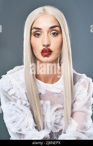 Ich höre immer noch zu, als ob ich eingeschlafen bin. Porträt einer attraktiven jungen Frau mit leuchtend dramatischen roten Lippen vor grauem Hintergrund. Stockfoto