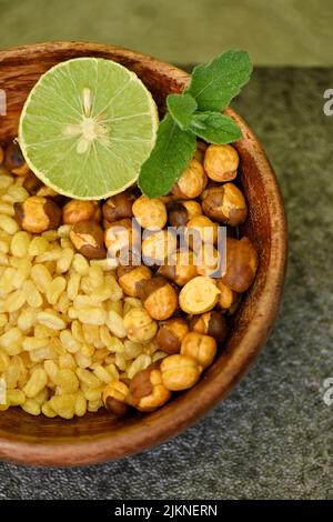 Nahaufnahme der gebratenen gelben Gramm Split Linsen mit schwarzem Gramm und in Scheiben geschnittene Zitrone, Minze in der roten Holzschale über unscharfem graubraunen Hintergrund. Stockfoto