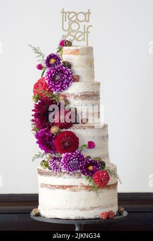 Eine vertikale Aufnahme eines großen, 4-stufigen Kuchens mit farbenfrohen, frischen Blumen auf weißem Hintergrund Stockfoto