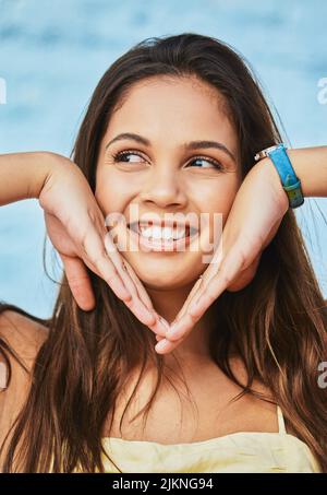 Dieses Gesicht sagt, dass sie den Sommer liebt. Eine attraktive junge Frau, die draußen vor blauem Hintergrund posiert. Stockfoto