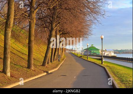 Jaroslawl, Russland, 05.08.2022. Wolga-Ufer am Morgen. Eine Straße mit einer Allee von Bäumen, eine Brücke in der Ferne Stockfoto