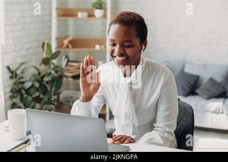 afroamerikanische Frau, die im Büro sitzt und auf einem virtuellen Meeting mit der Webcam Hallo sagt. Schöne schwarze Frau. Videoanruf der E-Learning-Zoom-App Stockfoto