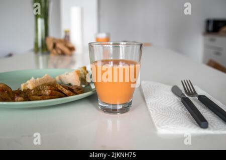 Bild von Glas Salmorejo-Creme typisch spanisches Gericht mit grünem Teller Brot und Tomaten auf einem eleganten weißen Küchentisch neben dem Besteck Stockfoto