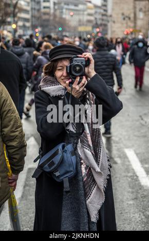 Bild von Mädchen, die Spaß haben, Foto mit DSLR-Kamera in einer überfüllten Straße mit Black Coat und Beret zu machen. (Vertikales Foto) Stockfoto