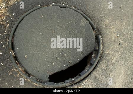 Loch in Asphalt. Luke in Masse. Kaputte Abdeckung. Gefährlicher Ort auf der Straße. Grube in Asphalt. Stockfoto