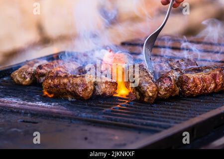 Preparing meat rolls called mici or mititei on barbecue. close up of grill with burning fire with flame and smoke. Stock Photo