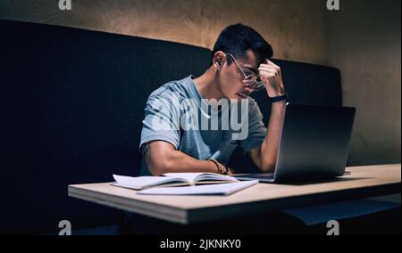 Diese Arbeit ist so stressig. Ein junger Geschäftsmann, der gestresst erscheint, während er seinen Laptop benutzt, um zu arbeiten. Stockfoto