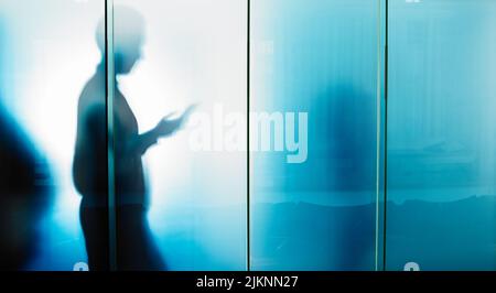 Arbeit hinter den Kulissen. Eine unkenntliche Silhouette eines Geschäftsmanns an einer Glaswand in seinem Büro. Stockfoto
