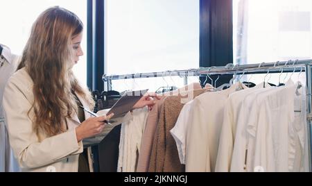 Eine junge Frau, die sich in einer Boutique Notizen von Kleidung macht. Stockfoto