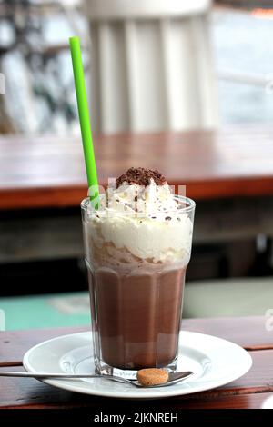 Eine vertikale Aufnahme von Schokoladenmilchshake mit Eis auf weißem Teller mit Löffel in verschwommenem Hintergrund Stockfoto
