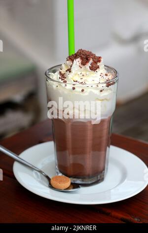Eine vertikale Aufnahme von Schokoladenmilchshake mit Eis auf weißem Teller mit Löffel in verschwommenem Hintergrund Stockfoto