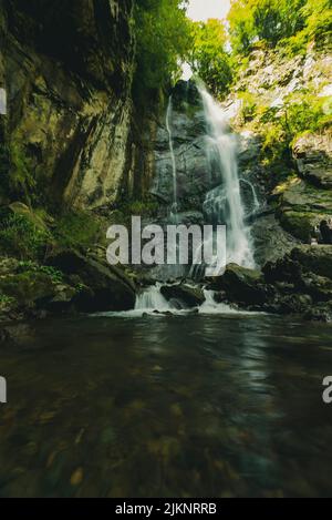 Ein natürlicher Blick auf einen Wasserfall, der an einem sonnigen Tag flussabwärts fließt Stockfoto