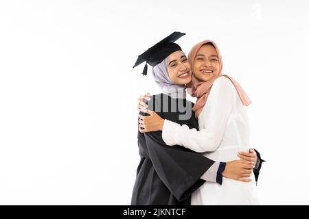 Asiatische weibliche Graduiertenschülerin trägt Toga umarmt ihre Schwester Stockfoto