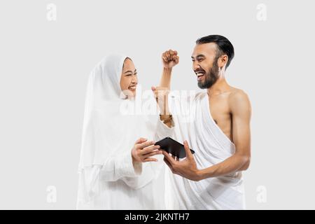 Glückliches Paar in Ihram-Kleidung, das Video mit dem Smartphone ansieht Stockfoto
