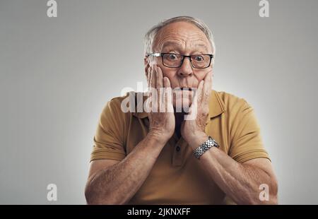 Es kann nicht wahr sein. Studioaufnahme eines älteren Mannes in Unglauben vor grauem Hintergrund. Stockfoto