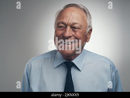 Ich habe mein Imperium gebaut, es ist an der Zeit, es zu genießen. Ein älterer Geschäftsmann, der tagsüber allein vor grauem Hintergrund im Studio stand. Stockfoto