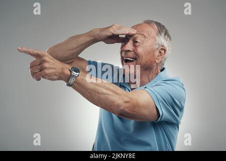 Ich sehe dich dort drüben. Ein älterer Mann mit der Hand, die sein Gesicht bedeckt und in einem Studio vor grauem Hintergrund in die Ferne blickt. Stockfoto