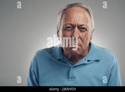 Du machst mich so wütend. Ein alter Mann schaut wütend auf die Kamera in einem Studio vor grauem Hintergrund. Stockfoto