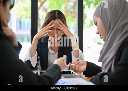 Gestresste und seriöse junge asiatische Geschäftsfrau oder Führungskraft, die mit dem Projekt ihres Mitarbeiters unzufrieden ist und sich während des Meetings unzufrieden fühlt. Stockfoto