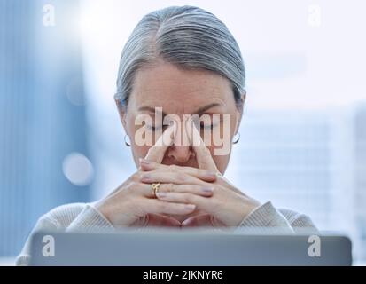 Wie viele Stunden habe ich hier gesessen, eine reife Geschäftsfrau, die allein im Büro sitzt und sich gestresst fühlt. Stockfoto