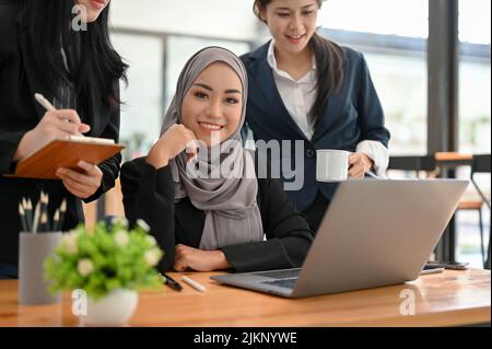 Schöne junge asiatische muslimische Geschäftsfrau oder weibliche Büroangestellte, die mit ihrem Team im Büro arbeitet. Stockfoto