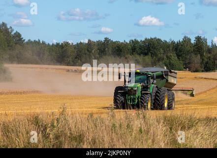 Eine schöne Aufnahme eines Traktors auf einem Grasfeld während der Ernte in Schweden mit grünen Bäumen an einem sonnigen Tag Stockfoto
