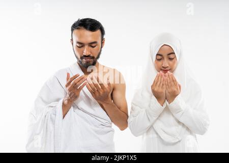 Pärchen trägt Ihram-Kleidung und betet vor isoliertem Hintergrund zu Allah Stockfoto