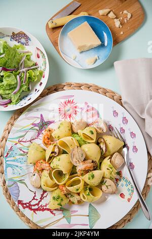 Eine vertikale Aufnahme von Pasta mit Meeresfrüchten mit Salat und Käse auf der Seite Stockfoto