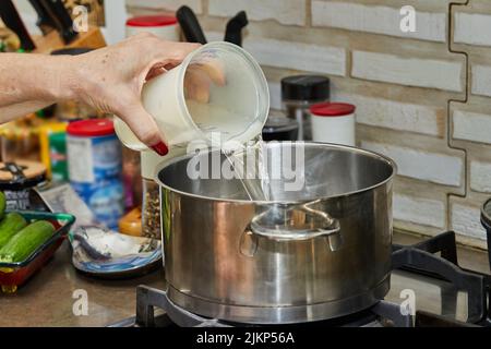 Der Koch gießt Wasser aus dem Messbecher in den Topf-Ofenofen. Stockfoto
