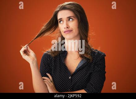 Gelangweilt von dieser Farbe, ist es an der Zeit sich zu ändern. Eine attraktive junge Frau, die allein vor rotem Hintergrund im Studio steht und ihre Haare berührt. Stockfoto