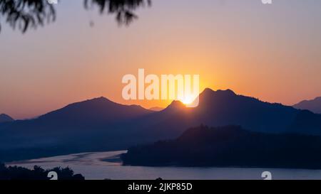 Eine wunderschöne Aussicht auf den Sonnenuntergang, die sich auf einem Flusswasser mit einer Silhouette von Bergen widerspiegelt Stockfoto