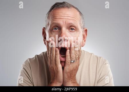 Oh, das ist eine Katastrophe. Ein hübscher reifer Mann, der allein vor grauem Hintergrund im Studio steht und schockiert aussieht. Stockfoto