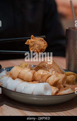 In einem kantonesischen Restaurant in Macau, China, werden in Nahaufnahme Chopsticks mit gedämpften Knödeln und Reisnudelrollen serviert Stockfoto