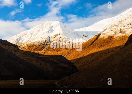 Eine schöne Aufnahme der wilden Landschaft im Schatten im Hintergrund von schneebedeckten Berggipfeln. Stockfoto