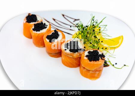 Sushi-Rollen aus rotem Fisch mit schwarzem Kaviar auf einem weißen Teller. Stockfoto
