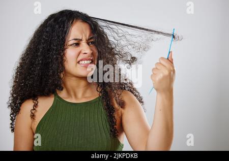 Warum muss das immer so ein Kampf sein. Eine Frau runzelte die Stirn, während sie ihr Haar vor einem grauen Hintergrund kämmte. Stockfoto