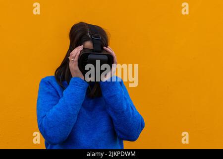 Porträt einer jungen Frau mit einem Blick aus Angst oder Verwirrung in einer Virtual-Reality-Brille auf gelbem Hintergrund Stockfoto